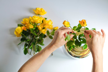 A woman arranging yellow roses in a vase