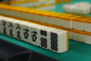 The bones (tiles) for the mahjong lie on the green table, the back and side plan is blurred. Table traditional game of Asia. - obrazy, fototapety, plakaty