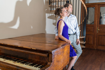 Old-fashioned forte piano with young man and woman pianist standing together in formal dress in...