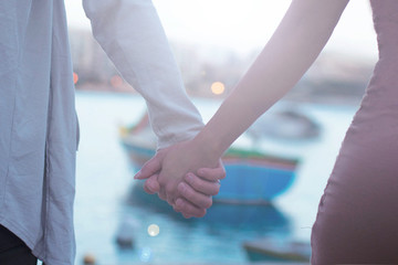 close up of couple holding hands, having date walking in Malta with traditional boat on background,love concept