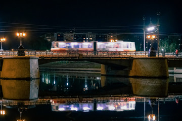 tram rides over a bridge in a night city