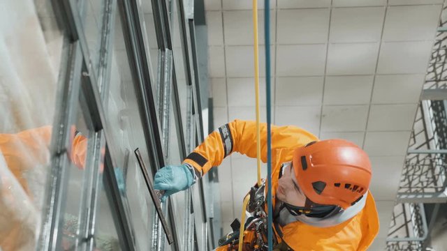 professional industrial climber window cleaner in helmet and rubber gloves washes windows on a tall building top view camera movement