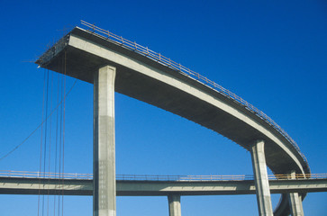 Fototapeta premium A concrete freeway structure ends abruptly with iron support structures sticking out and safety rails lining the top edge until further construction is continued, USA