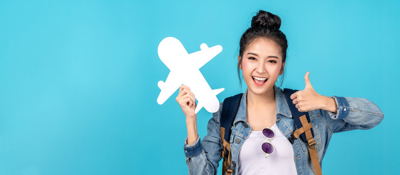 Young asian teenage backpack girl in concept of ready to travel abroad with white paper airplane in hand and positive smile to camera. Fit to fly service and travel plan after post covid coronavirus.