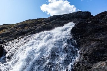 Sunny white scenic norwegian powerful river cascade waterfall with dark rocks and bright blue sky. Nature travel clean falling water landscape