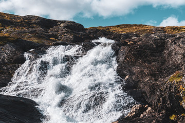 Sunny white scenic norwegian powerful river cascade waterfall with dark rocks and bright blue sky. Nature travel clean falling water landscape
