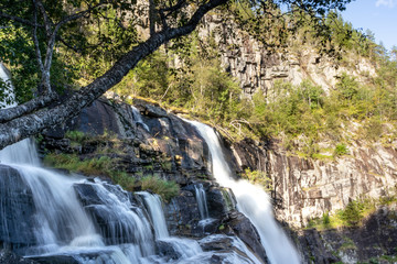 Skjervsfossen waterfall top part close white water view. Sunset colourful nordic summer natural landmark. Long exposure falling water with green trees