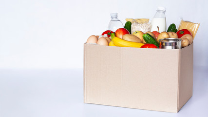 Various grocery items in cardboard box on gray table. Food box with fresh vegetables, fruits,...