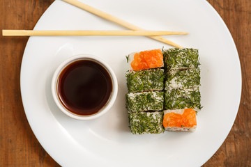 Set of rolls with dill and salmon on a white plate with soy sauce.