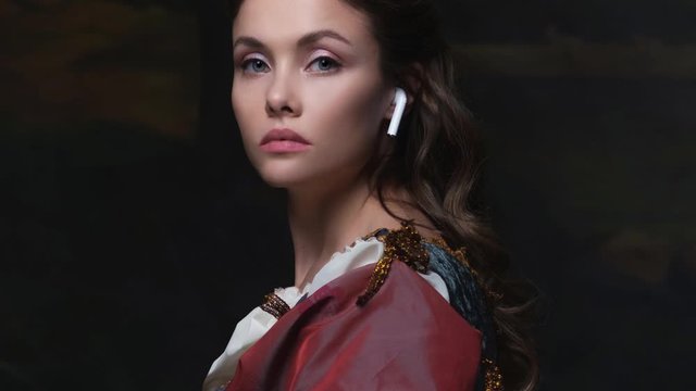 Old and new, concept. Portrait of a girl with a wireless earphone. Beautiful young Renaissance style woman
