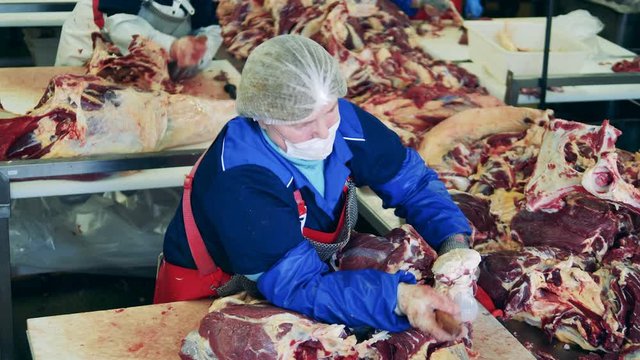 Female worker is carving a bone out of a piece of meat