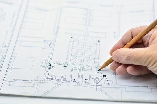 Mano dibujando con un lápiz en un plano de arquitectura de una casa