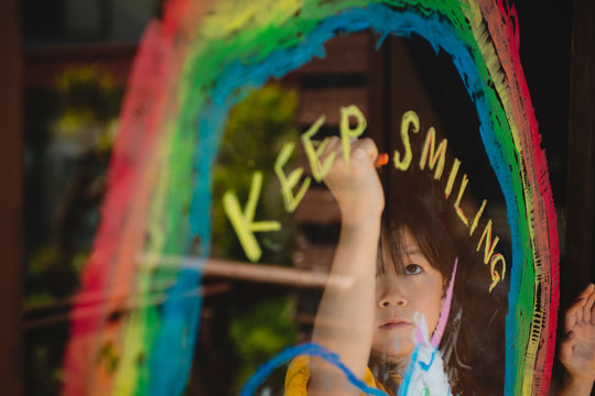 虹とユニコーンの絵と”KEEP SMILING”の文字を描く少女