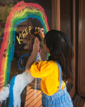 虹とユニコーンの絵と”KEEP SMILING”の文字を描く少女