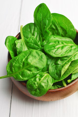 Green spinach leaves in dark wooden bowl on white wooden background. Vegan food lifestyle concept.