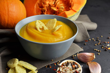 Pumpkin soup in a ceramic bowl with fresh pumpkins, garlic, wheat croutons and spices. Traditional thanksgiving day meal