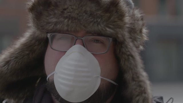 A man in a trapper hat turns to the camera and removes a face mask.