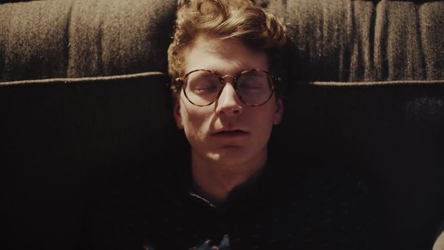 A young man opens his eyes and leaves the couch; an idea has come to him. 

Tripod. Fixed Focus. Medium-Close-Up. Cinematic. Performance. 23.976 FPS.