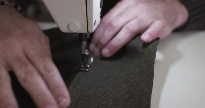 Close view of tailor's hands stitching a row on a fabric with a sewing machine