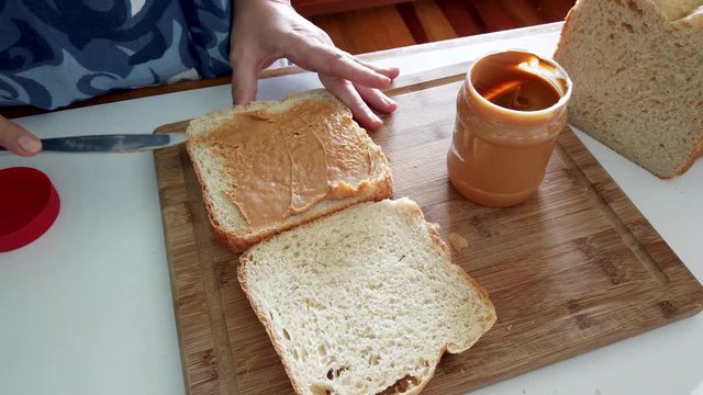 Woman spreading peanut butter on slice of homemade bread to make sandwich