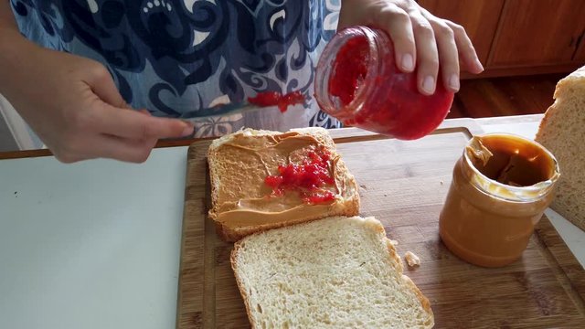 Hands spread strawberry jam on peanut butter and jelly sandwich