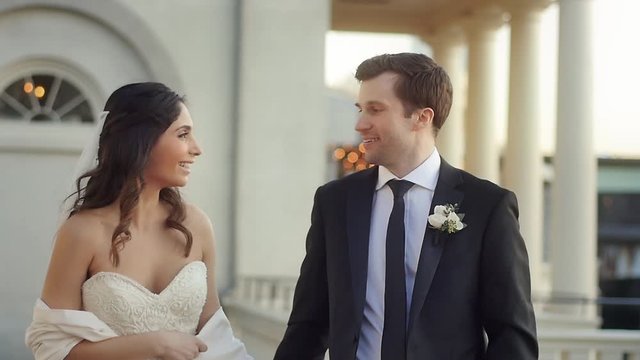 A newly married couple walk and kiss in slow motion in a pavilion