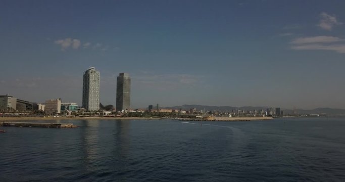 Aerial Dolly forward jet ski entering Port Olimpic Mapfre tower in distance