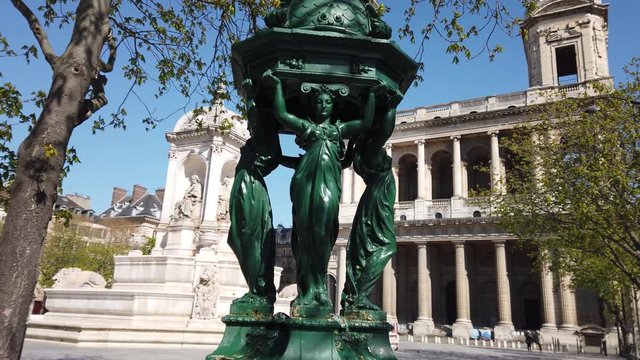 Wallace fountains with drinking water and beautiful sculptures in front of palace with old stone arches in Paris