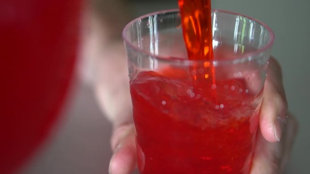 Pouring red drink into clear plastic cup.