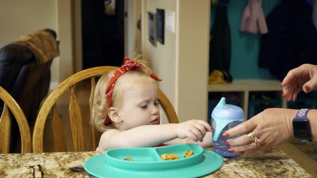 Girl toddler eats breakfast and drinks from a sippy cup at grandma's house