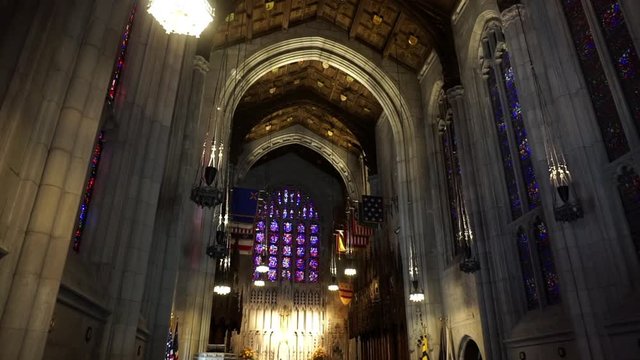 Cathedral interior with stained glass gothic windows, vaulted ceiling, carved wood ceiling panels, and flags.