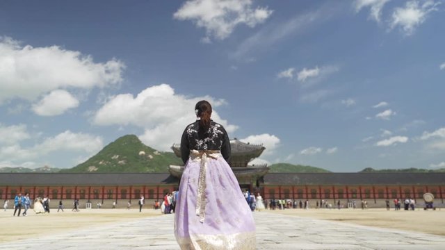 Girl in traditional Korean hanbok dress walking inside Gyeongbokgung Palace courtyard, wide shot in slow motion.