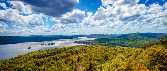 Fulton Chain Lakes view from the Adirondack Mountains in Upstate New York. Taken from the mountain summit after a short hiking trail. Lots of trees and clouds over the water. Camping in the Catskills - obrazy, fototapety, plakaty