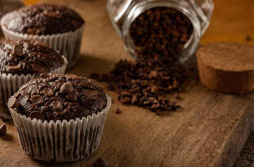 Chocolate cupcake with cacao nibs and chocolate drops in a wood table. Small cakes. Cupcakes