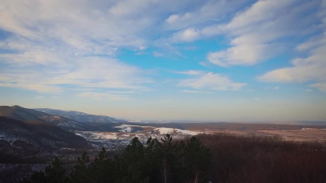 Panoramic view of mountains, a forest and trees under a blue sky with white clouds