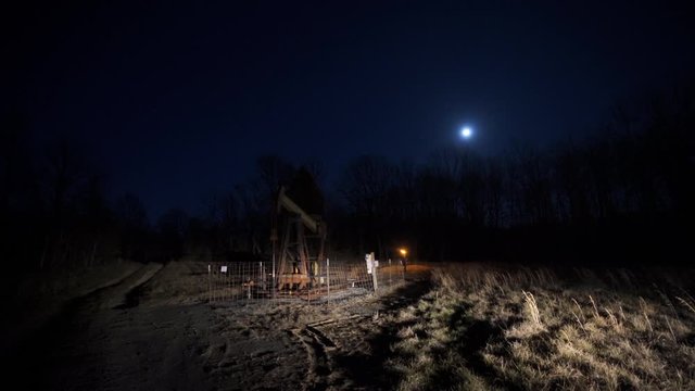 Wide shot of crude oil pump jack pumping during the night. Excess flare can be seen burning behind the pump.