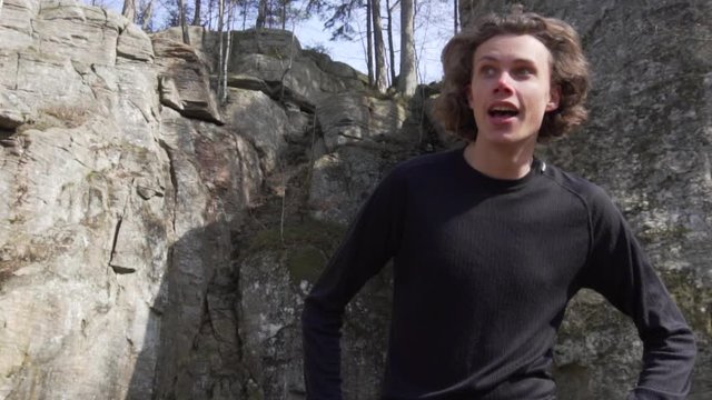 Young man runs and stops to catch breath in front of tall rocks in park, close up