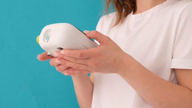 Low angle crop female interacting with handheld printer for making label and tag against bright blue background in studio