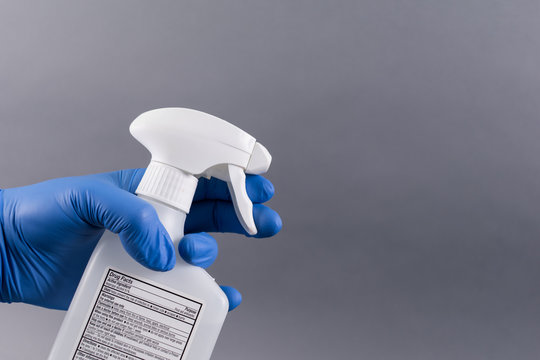 hand with blue glove holding disinfectant spray cleaning