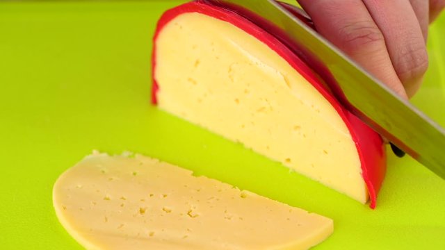Slicing A Dutch Edam Cheese On The Bright Green Cutting Board.- closeup shot