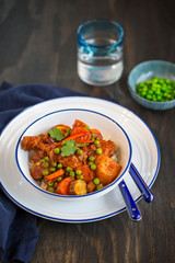 A bowl of Chicken and vegetable stew in tomato sauce served on rice on dark wooden background