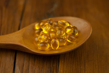 Fish oil capsules with omega 3 and vitamin D in a wooden spoon on wooden texture, healthy diet...