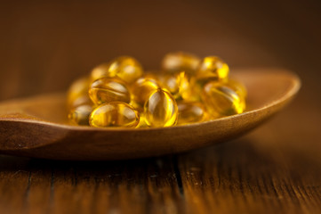 Fish oil capsules with omega 3 and vitamin D in a wooden spoon on wooden texture, healthy diet concept.