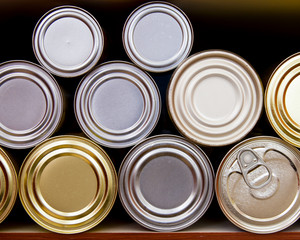 Many tin cans stacked on a pantry shelf in a row; hoarding or stocking up on canned goods in case...