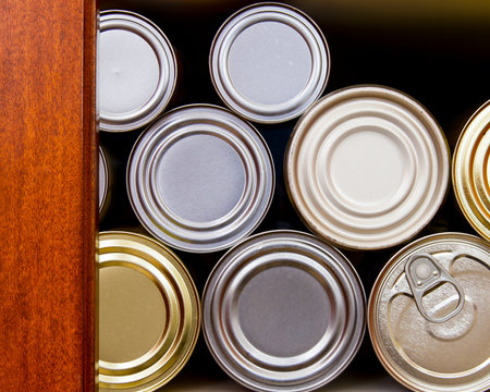 Many tin cans stacked on a pantry shelf in a row; hoarding or stocking up on canned goods in case of emergency