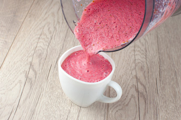 healthy eating, cooking, vegetarian food, dieting and people concept - close up blender and strawberries pouring milk shake to glass at home