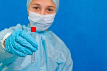 Female medical worker holding test tube on a blue background. Coronavirus test.