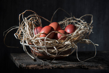Chicken eggs in a bowl with straw on an old partially rotted board in a dark barn. Shot in a low key.
