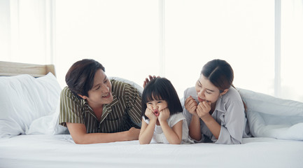 Fototapeta premium Happy asian family with a daughter are lying on bed under the blanket and Patting on daughter’s head in the bedroom