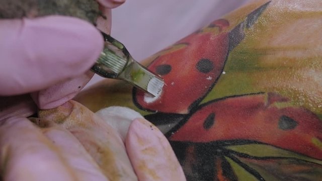 Needle tattoo machines inject a white ink into the skin of a girl. Close-up of the process of applying the tattoo on the skin. The girl puts an image of a ladybug on her skin. Color tattoo.